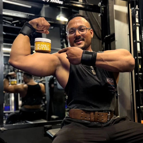 Man flexing his arm in a gym holding a container of Honey peanut butter