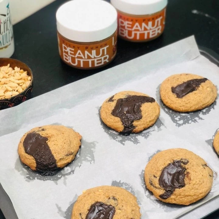 Cookies with chocolate filling on a baking sheet next to jars of peanut butter.